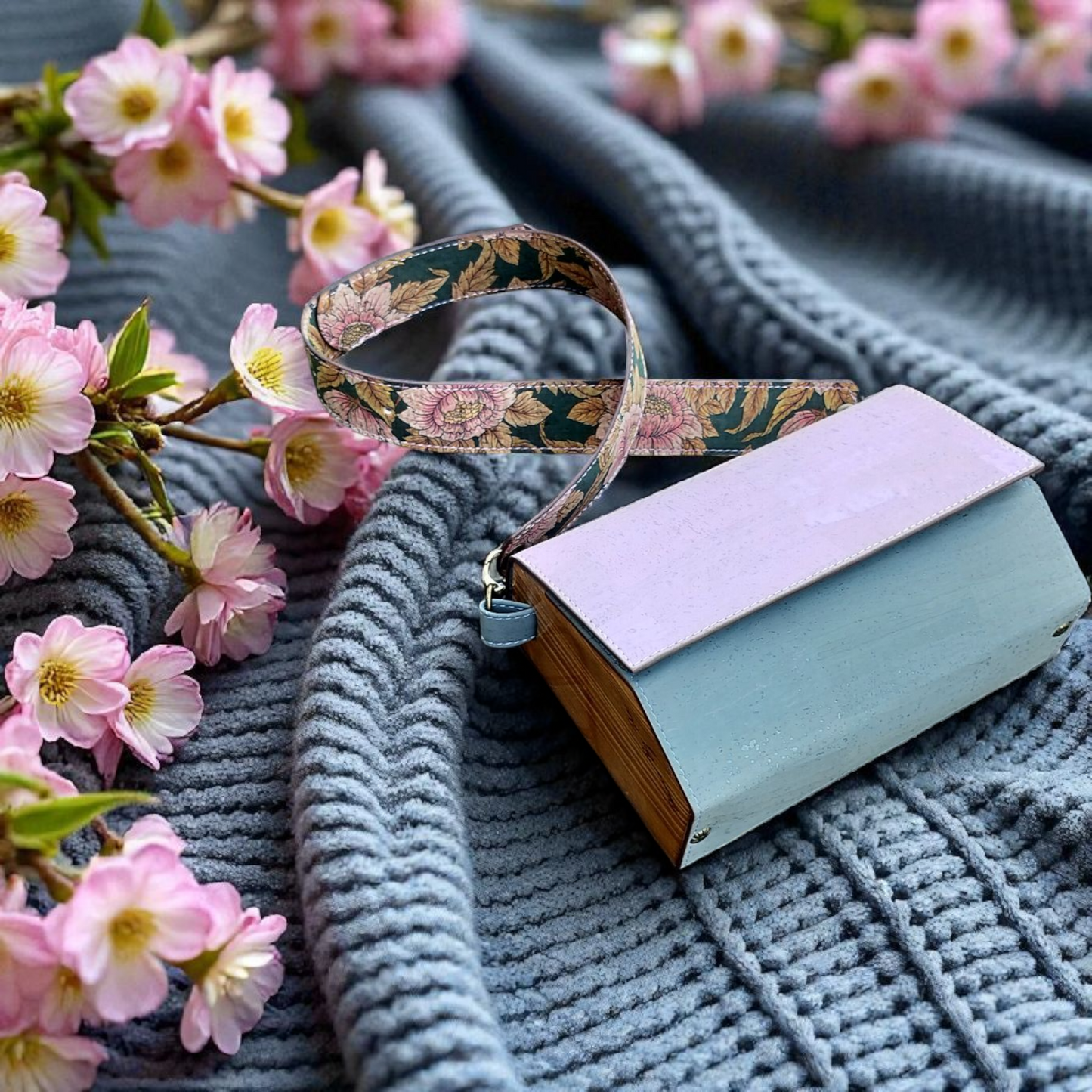 Small handbag with floral strap on a textured surface with cherry blossoms