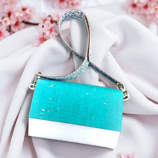 Turquoise handbag with white base on a pink fabric background with cherry blossoms