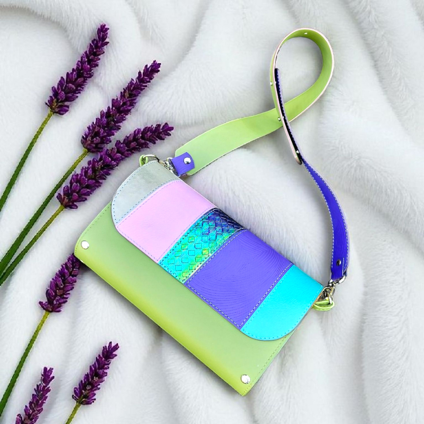 Colorful wristlet with a green strap and purple accents on a white fabric background with lavender flowers.